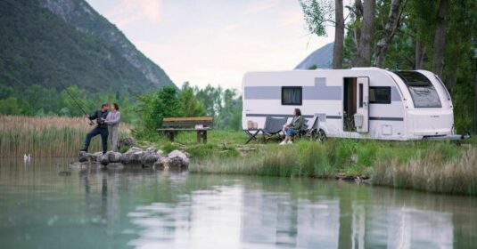 Folk koser seg nede ved vannet. Utenfor campingvogn.